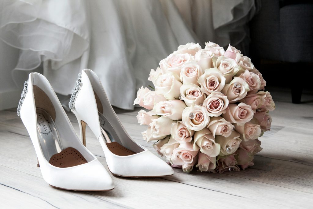 Weiße Brautschuhe und ein Strauß zarter Rosen.