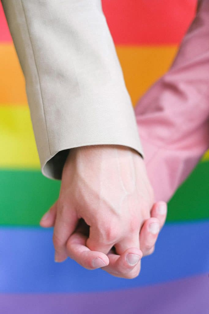 Zwei Menschen halten Händchen vor einer Regenbogenflagge des LGBTQ+-Pride.