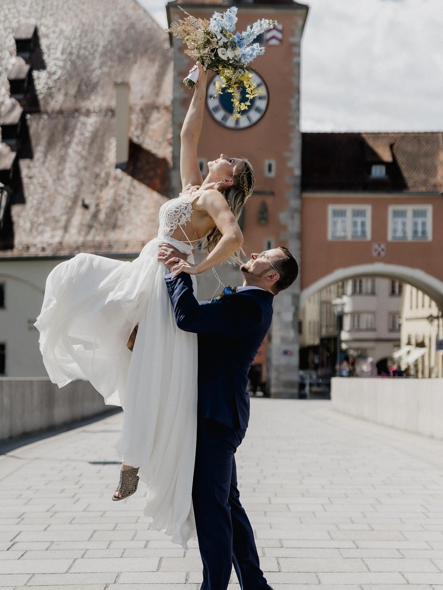 Braut und Bräutigam Philipp und Antje liegen freudig umarmt auf einer Brücke. Die Braut hält ihren Brautstrauß hoch.
