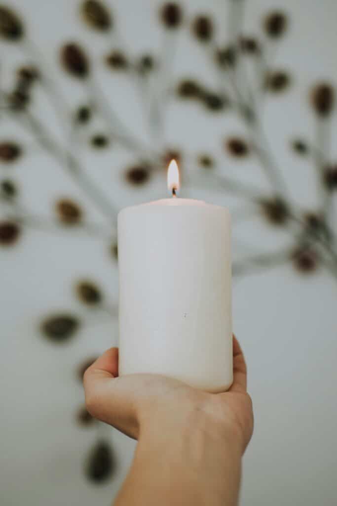 Hand hält eine brennende Kerze vor einem unscharfen Hintergrund aus getrockneten Blumen. Perfekt für eine rituelle freie Trauung.