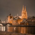 Nachtansicht des beleuchteten Regensburger Doms und der Altmühl, schneebedeckte Gebäude.