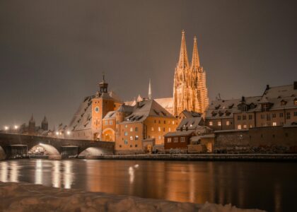 Nachtansicht des beleuchteten Regensburger Doms und der Altmühl, schneebedeckte Gebäude.