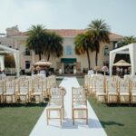 Vorbereitung einer freien Trauung im Garten mit weißen Stühlen und Blumenarrangements.