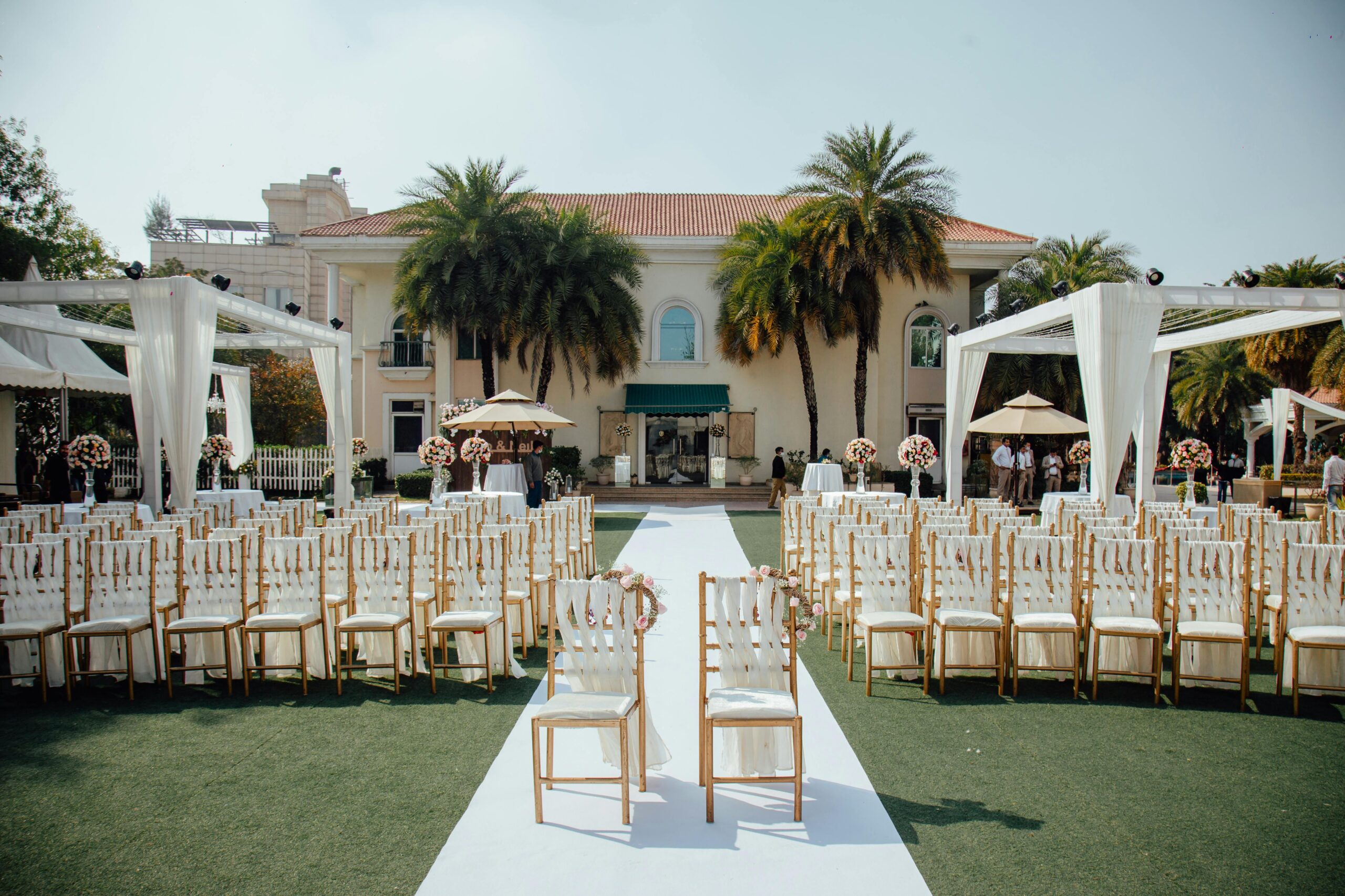 Vorbereitung einer freien Trauung im Garten mit weißen Stühlen und Blumenarrangements.