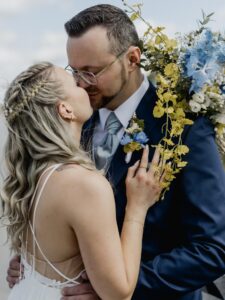 Paar küsst sich am Hochzeitstag mit blauem und gelbem Blumenstrauß