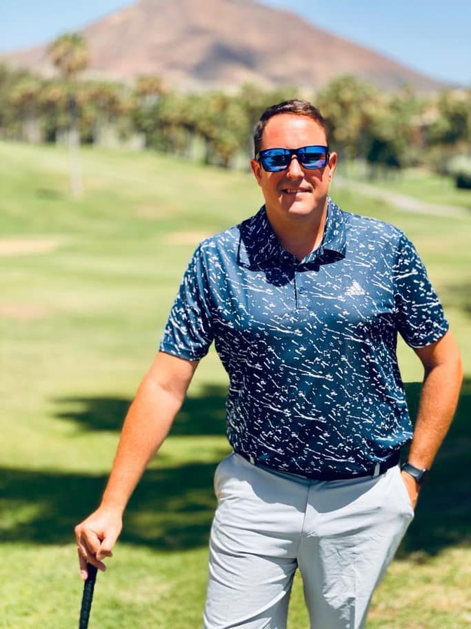 Mann mit Sonnenbrille hält einen Golfschläger auf einem sonnigen Platz