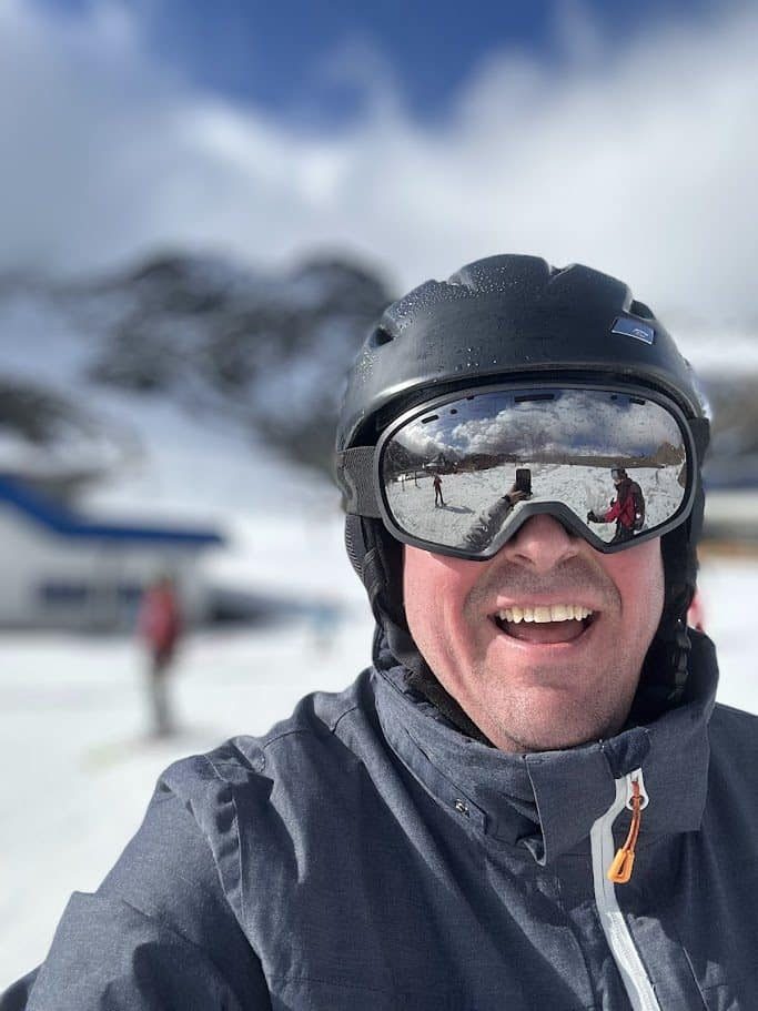 Glücklicher Mann mit Skibrille und Helm auf schneebedeckten Bergen