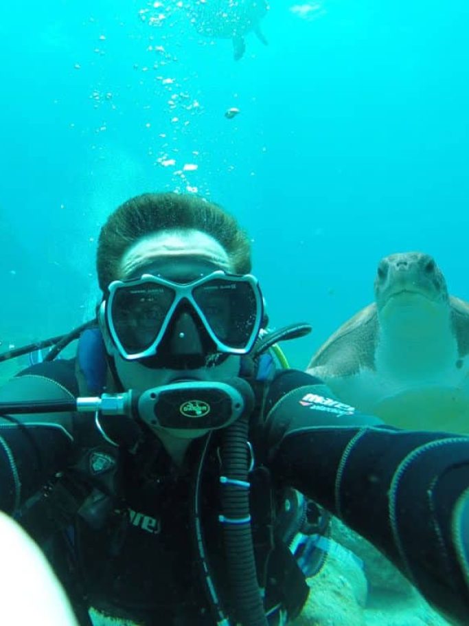 Ein Taucher macht unter Wasser ein Selfie mit einer Meeresschildkröte.